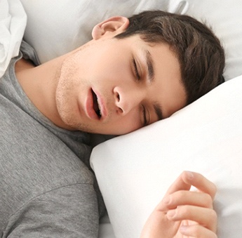 A young male wearing a gray t-shirt and breathing through his mouth while asleep