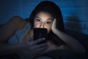 A woman using her phone in bed at night.