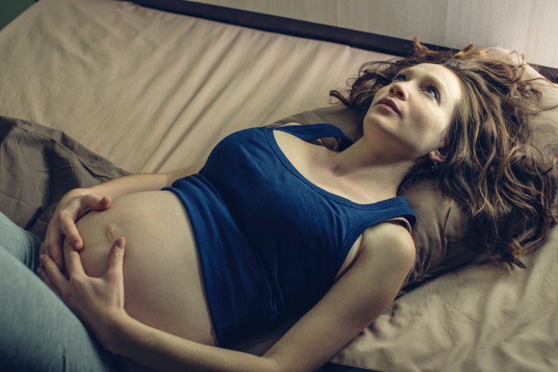 a pregnant woman lying in bed awake and holding her belly 
